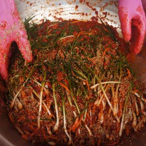 Bild på en person som blandar ingredienser av kryddning för fermentering av kimchi i en stor metallskål.