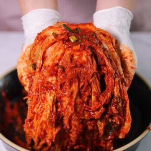 Bild på en person som masserar in en röd kryddpasta i kinakålens blad, där kryddningen täcker varje del.