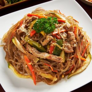 Bild på en tallrik med japchae, en koreansk nudelrätt med glasnudlar, nötkött och grönsaker.