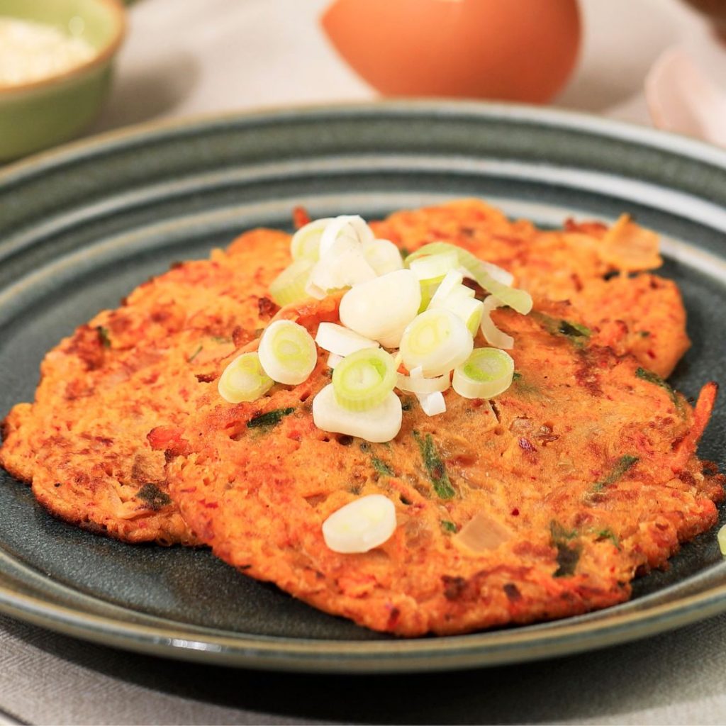 Bild på en tallrik med kimchi jeon, kimchipannkaka med en krispig yta och en fyllig, kryddig smak av kimchi och vårlök