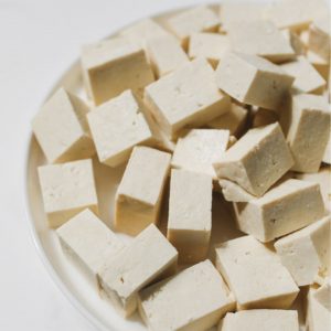 Bild på en tallrik med tofu, vit och fast i konsistensen, skuren i fyrkantiga bitar, och redo att användas i soppor eller stekas till krispighet Bild på en tallrik med tofu, vit och fast i konsistensen, skuren i fyrkantiga bitar, och redo att användas i soppor eller stekas till krispighet.