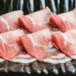 Bild på en tallrik med tunt skivad fläsk, jämna skivor med insprängt fett, redo för stekning eller grillning för en saftig och smakrik måltid.