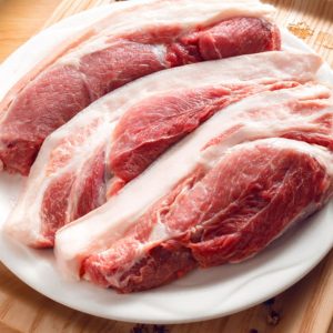 Bild på skivad rått fläskkött, rosa och marmorerat med fett, redo att tillagas för att ge en saftig och smakrik rätt