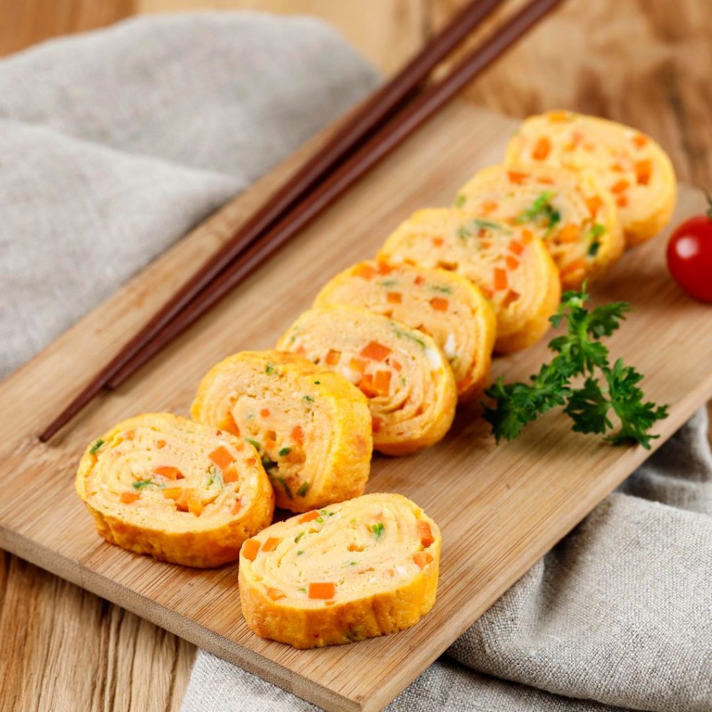 En bambu tallrik med gyeran mari, koreansk omelett rullad med grönsaker och ägg