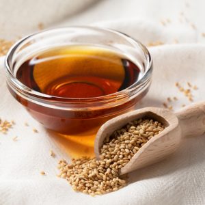 En bild på en skål av sesamolja, med den gyllene, aromatiska oljan tillsammans med sesamfrön på sidan.