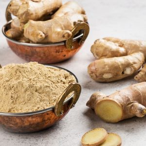 En bild på en skål med malen ingefära, ljusbrunt pulver med färsk ingefära vid sidan