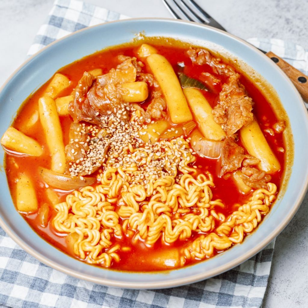 En djup tallrik med rabokki, koreansk tteokbokki blandad med ramen och kryddig sås.