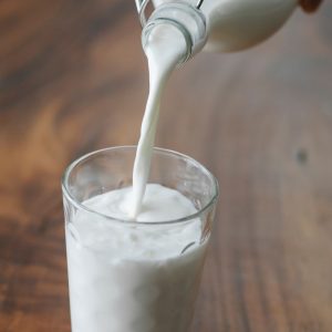 En flaska mjölk som hälls i ett glas, vit och krämig, redo att drickas eller användas i bakning.