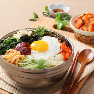 Bild på bibimbap med färgglada grönsaker, stekt ägg och nötkött, serverad på en bädd av ris och toppad med gochujang