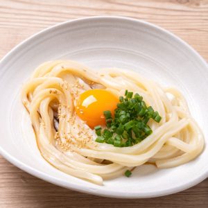En skål med kamatama udon, toppad med rå äggula och gräslök för en krämig och smakrik upplevelse En skål med kamatama udon, toppad med rå äggula och gräslök för en krämig och smakrik upplevelse