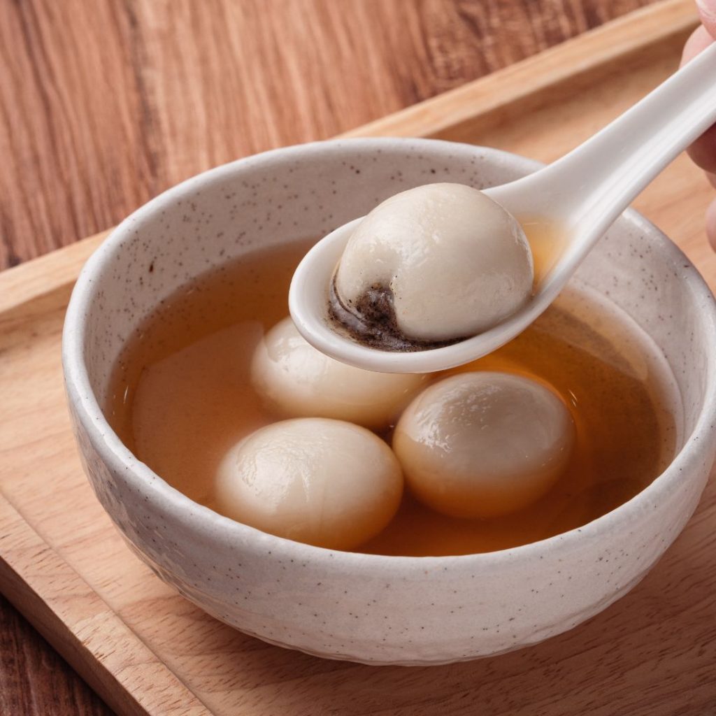 En skål med tangyuan, små, runda risklumpar med en fyllning av svart sesampasta, serverade i söt buljong
