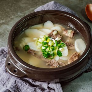 En skål med tteokguk, klar buljong med skivade tteok och garnering av salladslök och kött