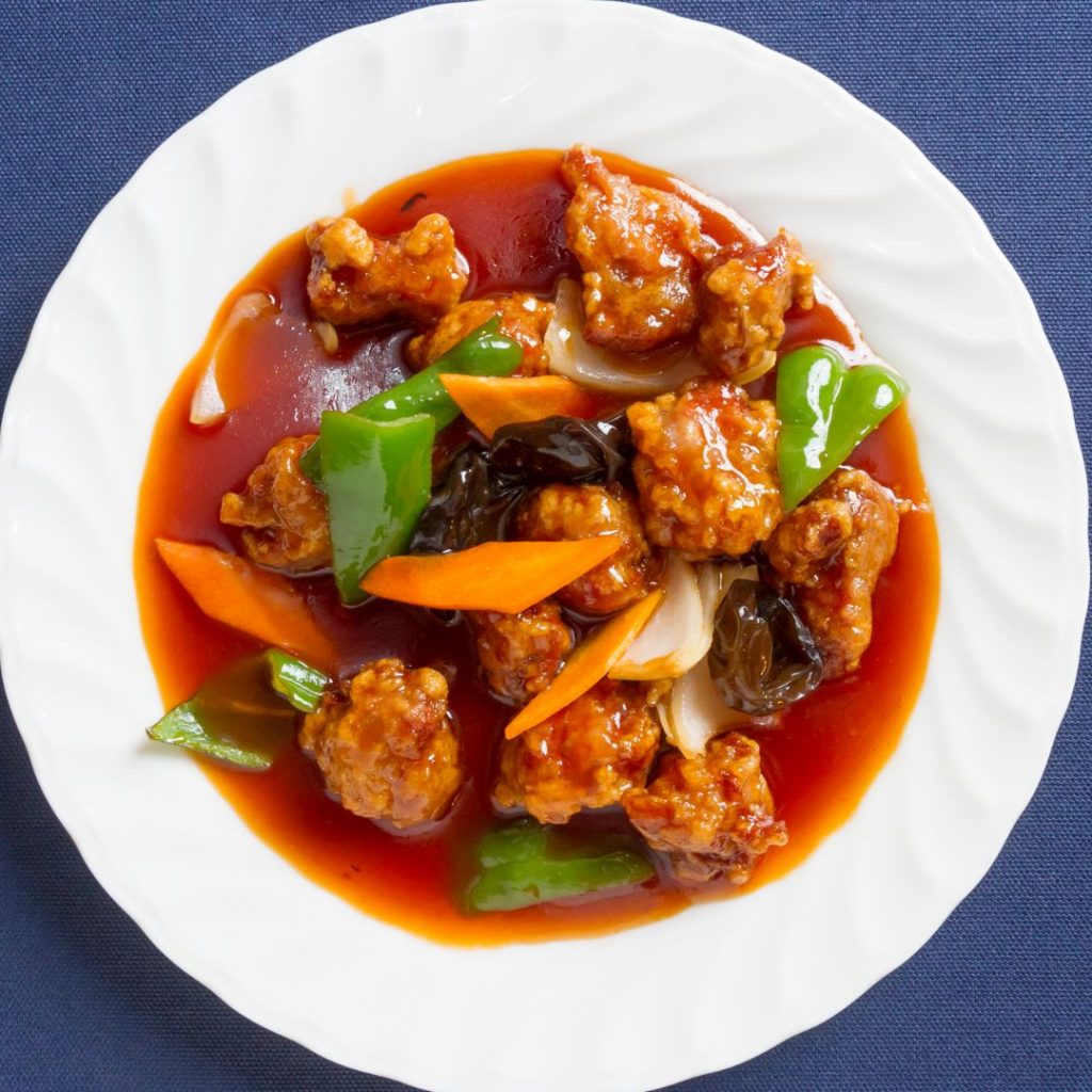 En tallrik med Gulaurao, kinesisk friterade fläskbitar i sötsur sås med en gyllene och krispig yta.