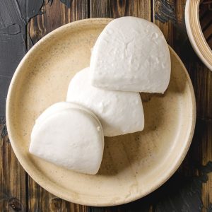 En tallrik med ångade bao buns, fluffiga, vita bröd redo att fyllas med olika ingredienser