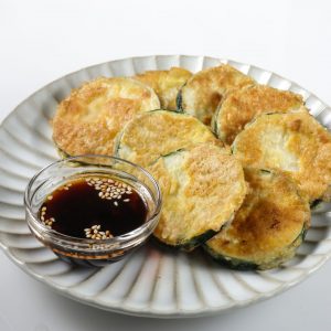 En tallrik med hobak jeon, koreanska zucchiniplättar gyllene stekta i en krispig smet med soja vid sidan