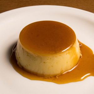 En vit tallrik med en Purin i mitten, krämig japansk karamellpudding, med en skinande karamellsås.