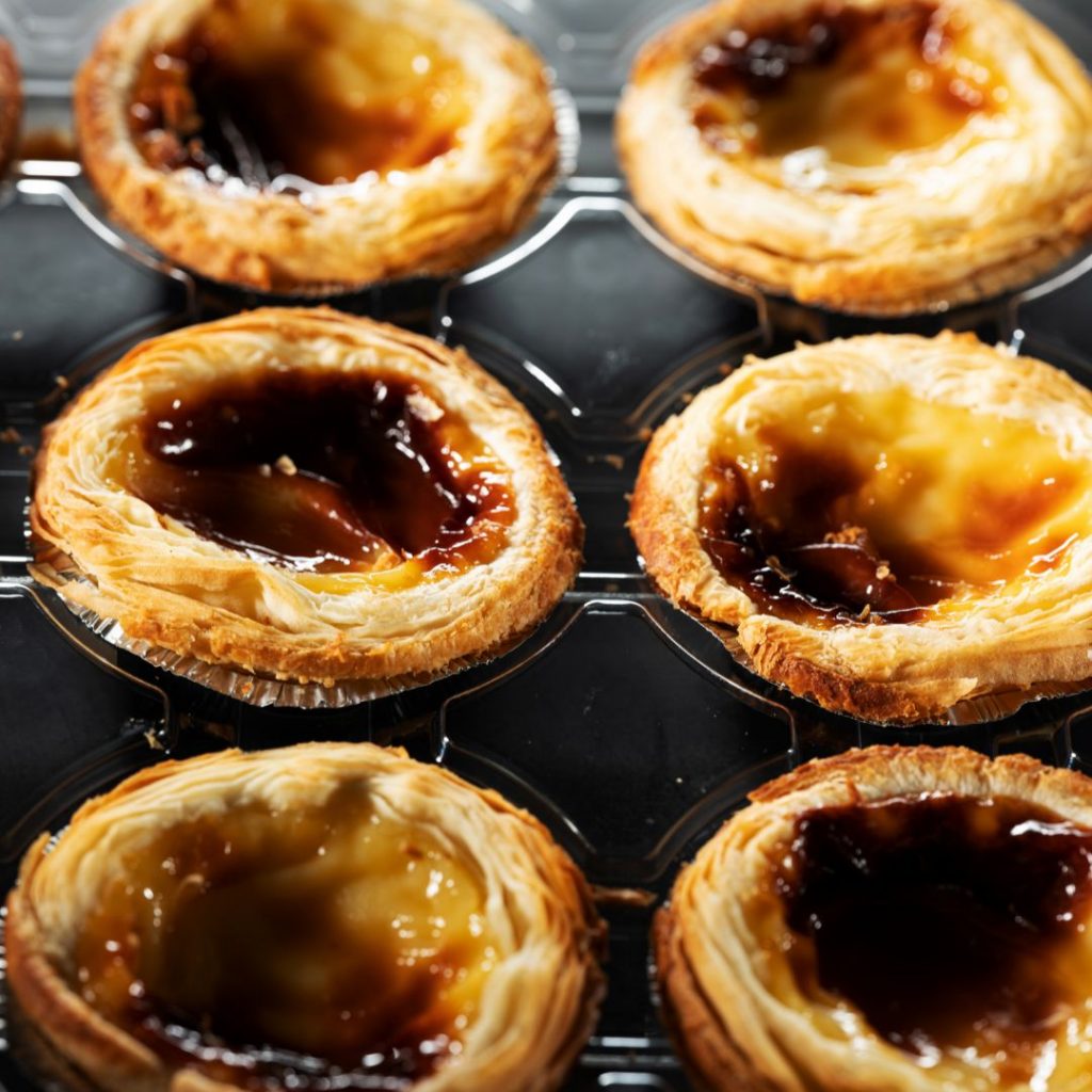 Ett dussin Macao egg tart, gyllene och krämig med ett sprött smördegsskal och len fyllning.
