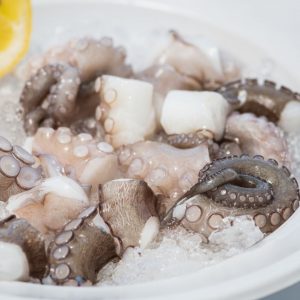Rå bläckfisk skärade i bitar, vita och mörade tentakler redo för stekning eller kokning.