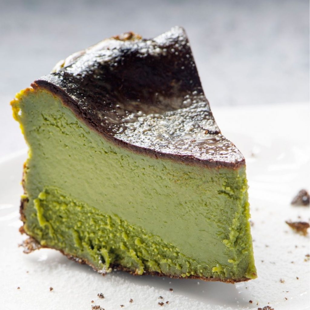 En bit av Matcha Basque cheesecake i jordaktig grön färg med en krämig kärna och bränd topp