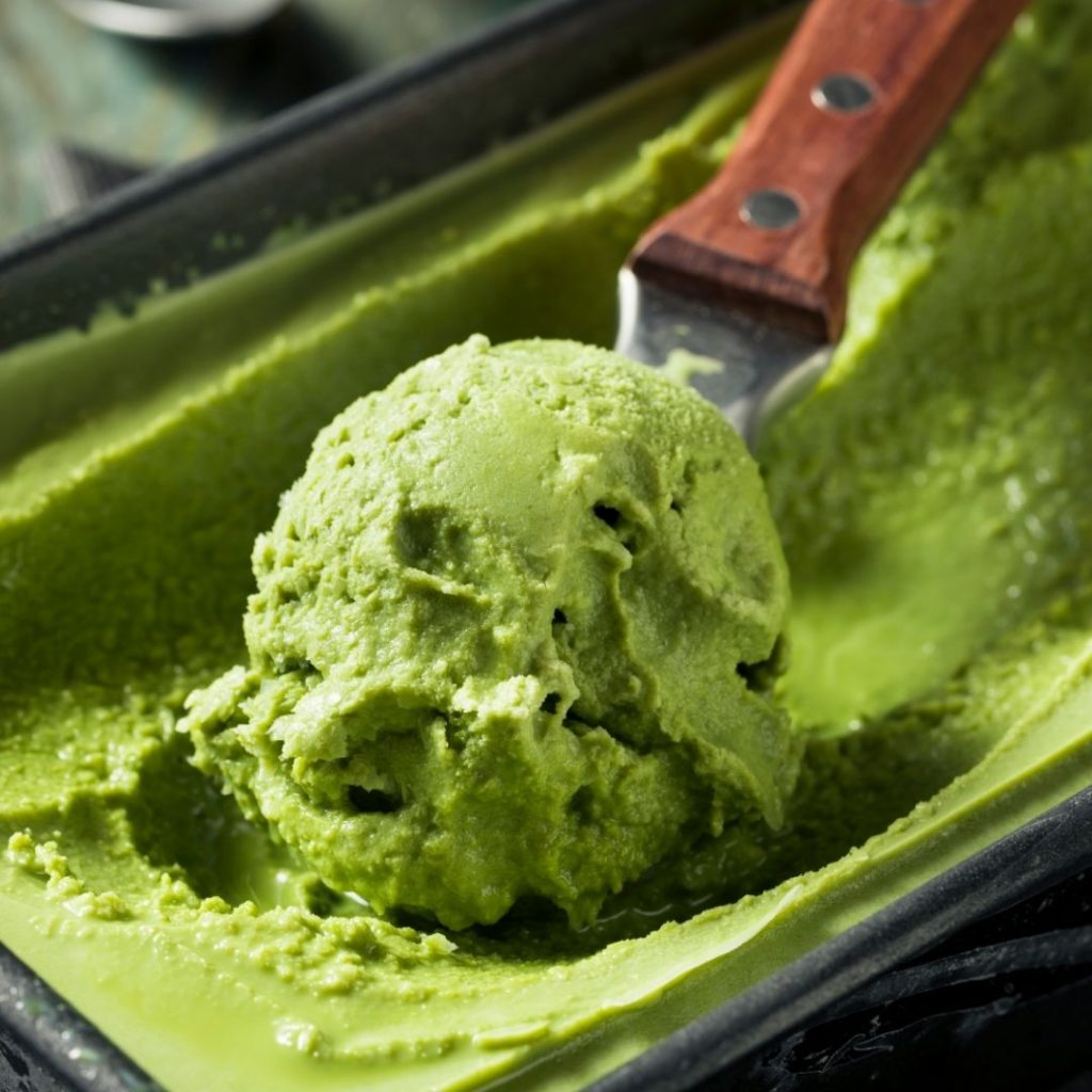 En brödform fylld med lysande grön matcha glass med en härlig jordisk smak, en glasskopa som skopar en kula