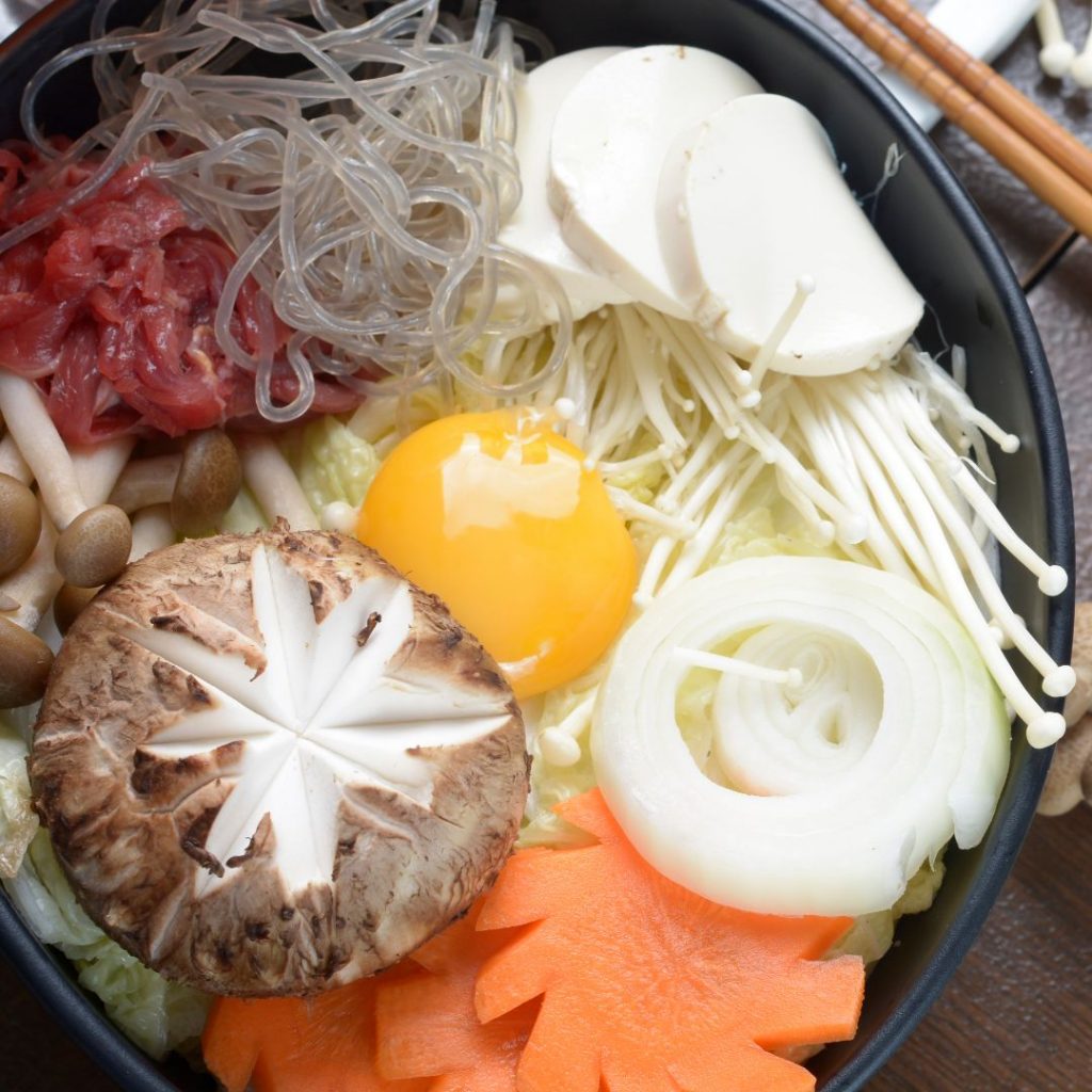 En gryta av Sukiyaki, en japansk hotpot med nötkött, tofu och grönsaker i en smakrik buljong.