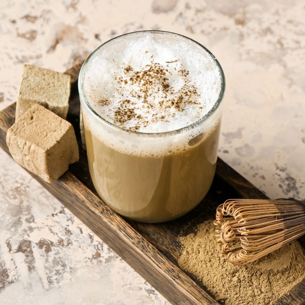 En kopp krämig hojicha latte med en mild rostig tesmak, med torr hojichapulver vid sidan.