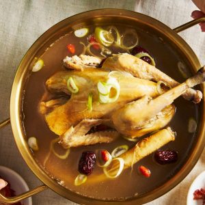En metallgryta med Samgyetang, koreansk ginsengkycklingsoppa, i klar buljong och torkade jujube.