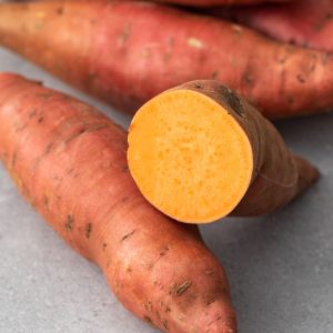 En par färska sötpotatisar, en del i hälften, mörkröd skinn och orange kött, perfekt för bakning eller rostning.