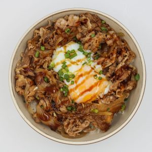 En skål med Gyudon, en skål med ris toppad med tunt skivat nötkött och lök i en sötsojasås och toppad med ett ägg.
