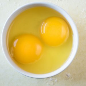 En skål med två råa ägg, med en gul äggula och klar genomsklinlig äggvita, redo för olika maträtter.