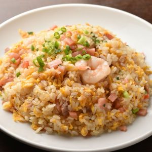 En tallrik med kinesisk Yangchow stekt ris, stekt i gyllene gul och fyllt med grönsaker, räkor och ägg.