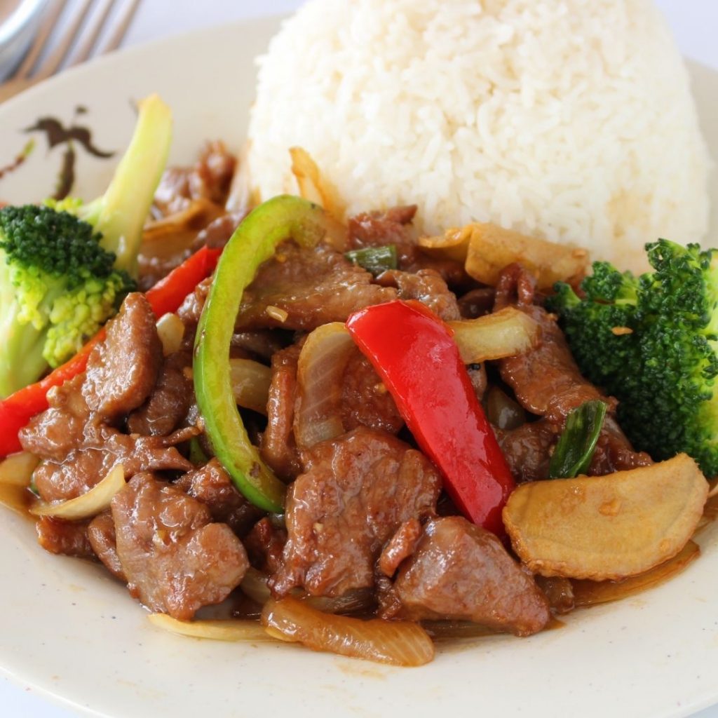 En tallrik med wokad biff med broccoli och paprika i en smakrik brun sojasås och vitt ris vid sidan.