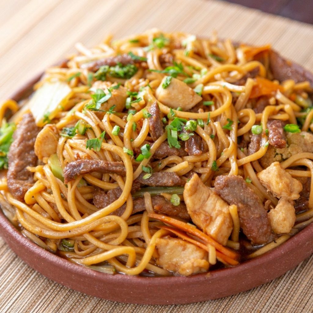 En tallrik yakisoba med stekta nudlar, färska grönsaker och kött i en mörk sojasåsbas.