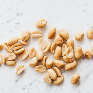 En hög med skalade saltade jordnötter med ljusbrun färg, liggande på ett marmorbord.