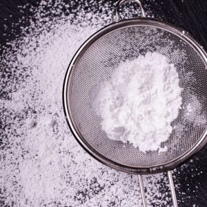 En liten sil med vitt florsocker i sig och spritt över ett svart underlag, perfekt för bakelser