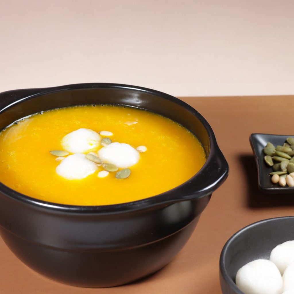 En skål med Hobakjuk, en len och söt gulorange gröt gjord på kabocha pumpa med risbollar