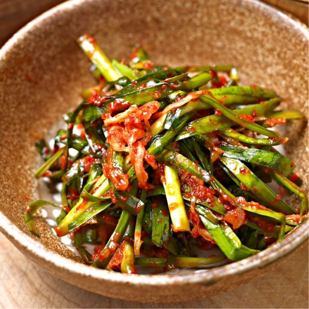En skål med koreansk pa-kimchi, fermenterade salladslökar täckta i kryddig gochugaru och vitlökspasta.