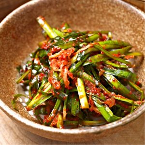 En skål med koreansk pa-kimchi, fermenterade salladslökar täckta i kryddig gochugaru och vitlökspasta.