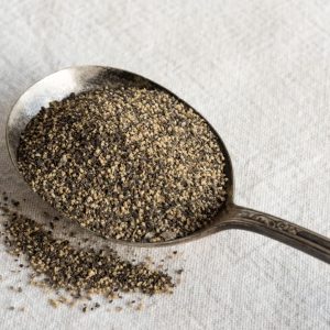 En sked fylld med aromatisk svartpeppar, redo att användas som en kryddig smakförstärkare i matlagning.
