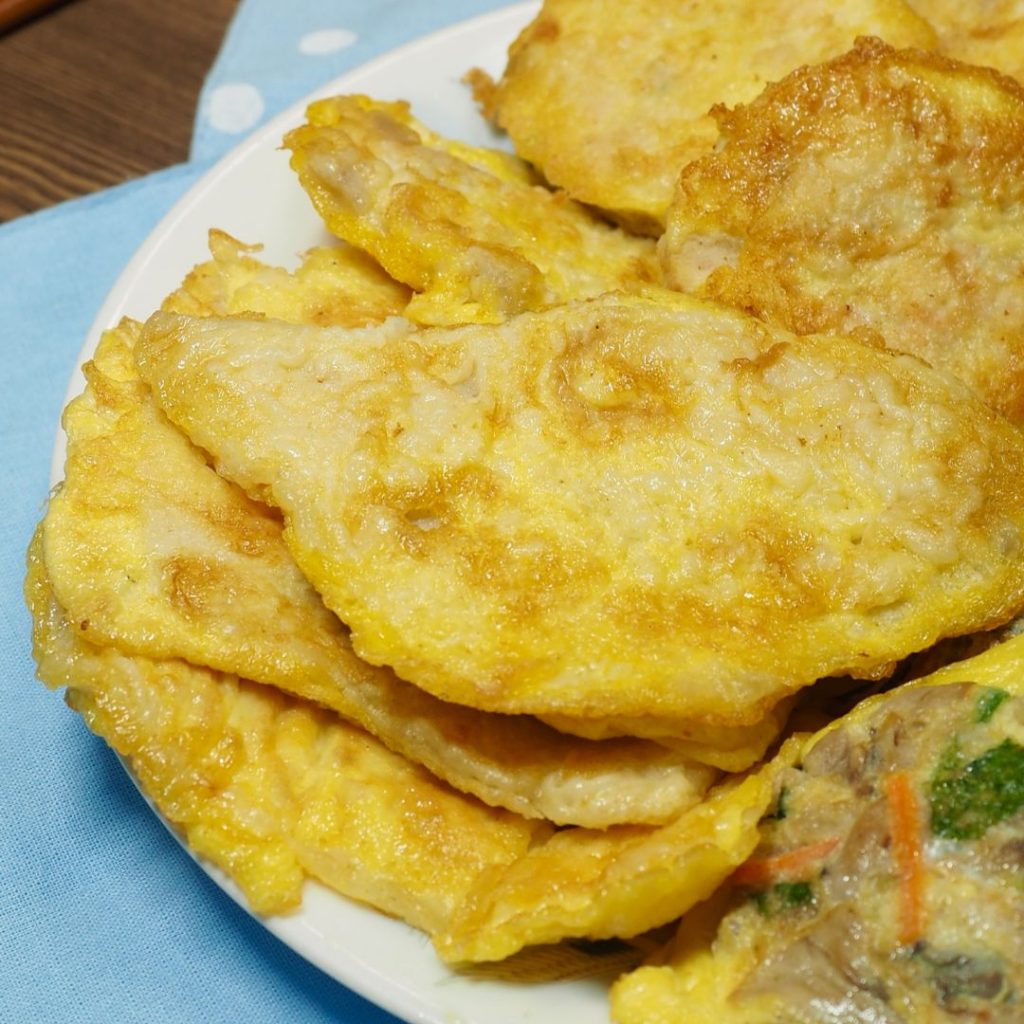 En tallrik med Dongtaejeon, stekta skivor av pollock fisk doppade i äggsmet, upplagda på ett fat som en koreansk banchan