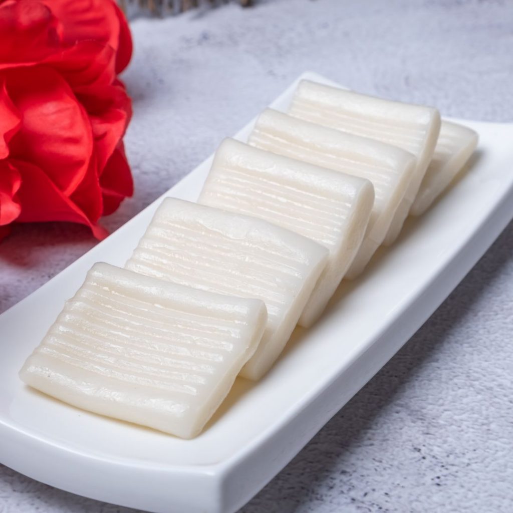 En tallrik med traditionell vit jeolpyeon, en koreansk pressad riskaka i dekorativ mönster, en festlig dessert