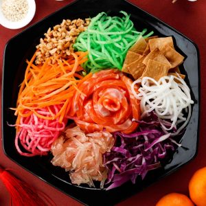 Ett fat med Yusheng, en färgstark sallad med rå fisk, grönsaker och krispiga tillbehör för god lycka