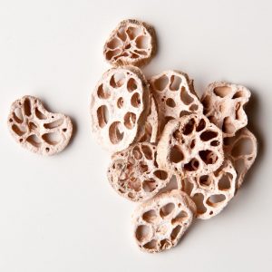 Tunna, torkade skivor av lotusrot liggande på vitt underlag, perfekta för asiatiska rätter