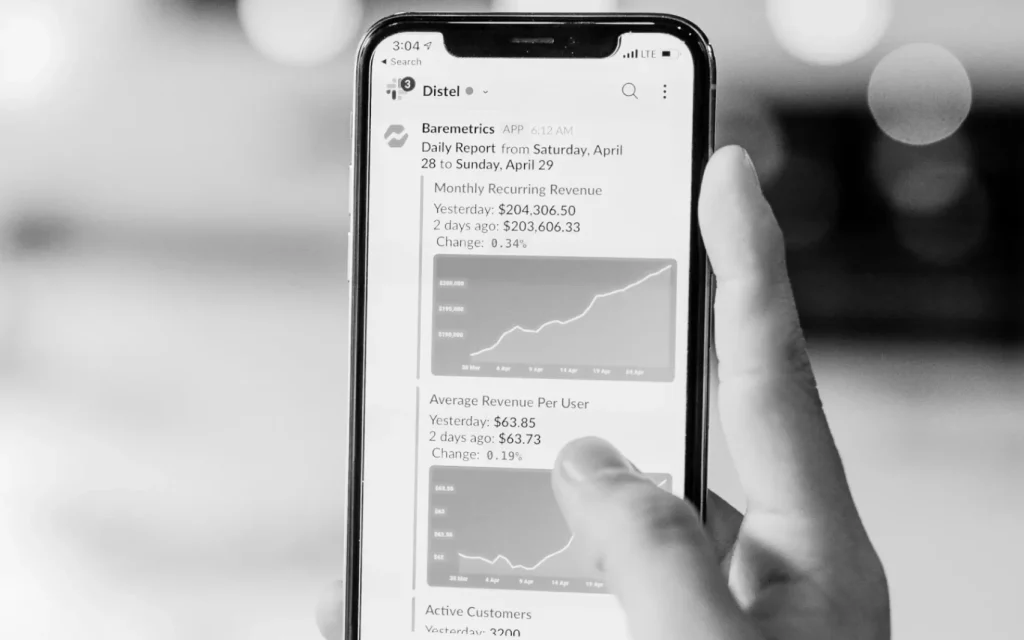 Person hält Smartphone in der Hand, in der Statistiken zu Umsatz zu sehen sind. Schwarz-Weiß
