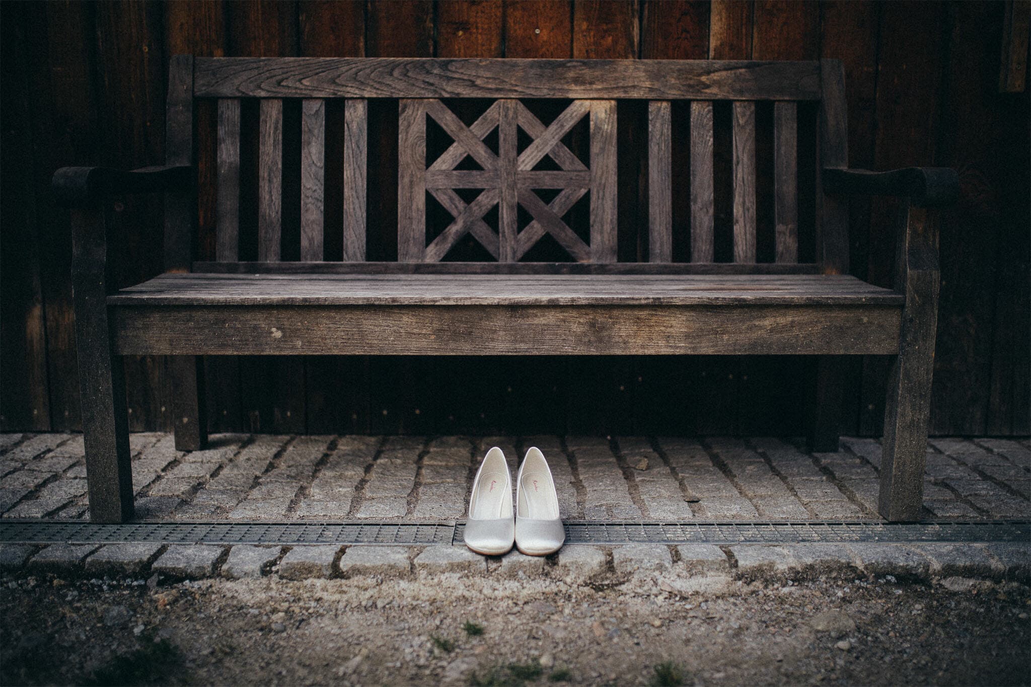 Elegante Brautschuhe vor einer hölzernen Parkbank, eingebettet in eine natürliche, ruhige Umgebung. Die Schuhe stehen im Fokus und symbolisieren den Beginn eines neuen Lebensweges.