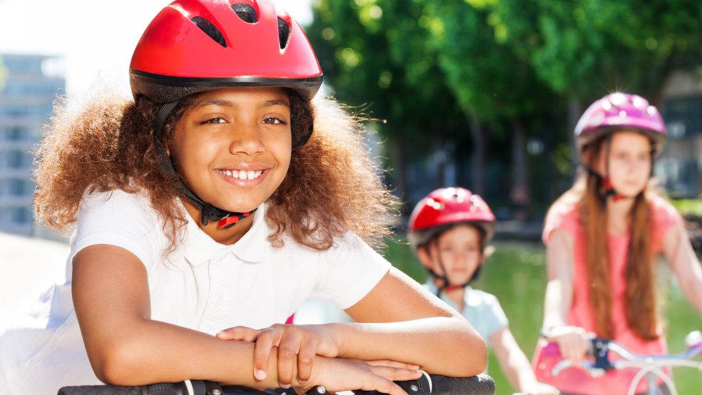 Tre unga tjejer står med sina cyklar i en somrig miljö.