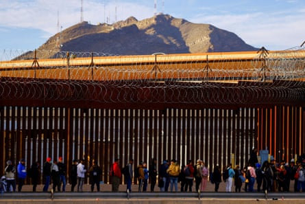 Migrants queue near the border fence, after crossing the Rio Bravo river, to request asylum in El Paso, Texas, on 5 January.