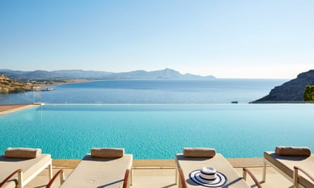 Sun loungers look out across a pool, then over a small ocean bay out to distant land.