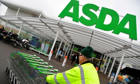 An Asda worker pushes shopping trolleys at a store in West London