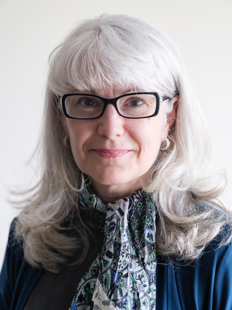 woman with glasses smiles at the camera in front of a plain background